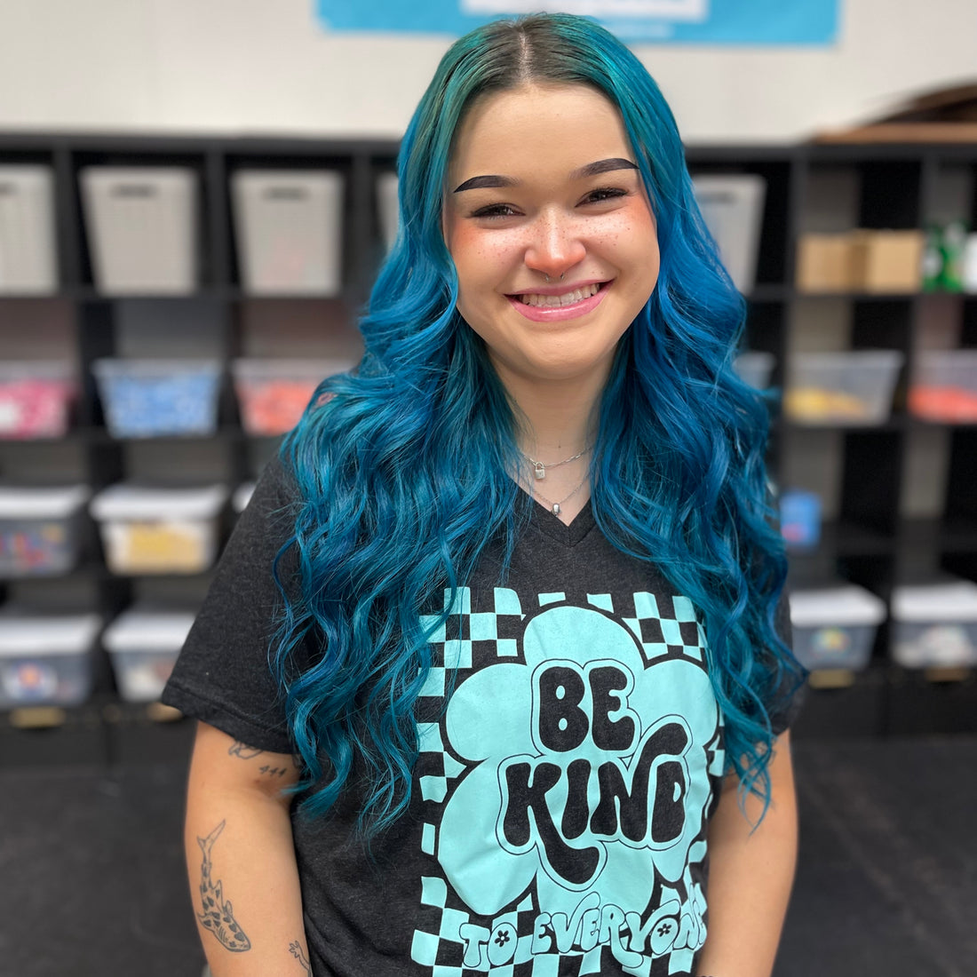 Sarah, modeling a medium in our Groovy Be Kind to Everyone® t-shirt that features an aqua design on a black tri-blend v-neck.