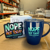 Our Nope Not Today Maybe Tomorrow coffee mug and magnet, on top of a box at the Shirt Shop.