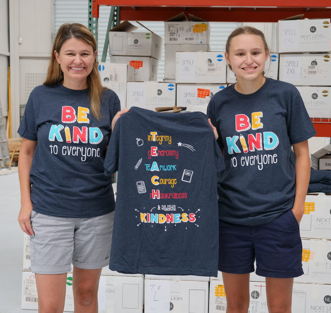 Jackie and Jordyn, at the shirt shop, displaying the back of our "T.E.A.C.H. Kindness" Be Kind to Everyone® short-sleeve tee.  The are both wearing smalls.