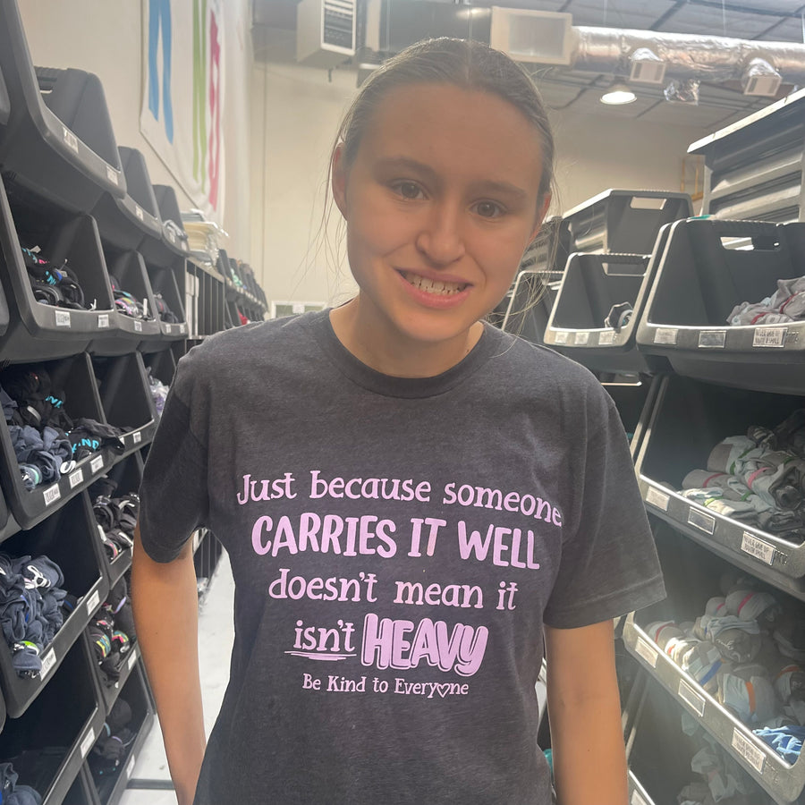 Jordyn, at the shirt shop, wearing our Carries it Well Be Kind to Everyone® short-sleeved t-shirt in a small.