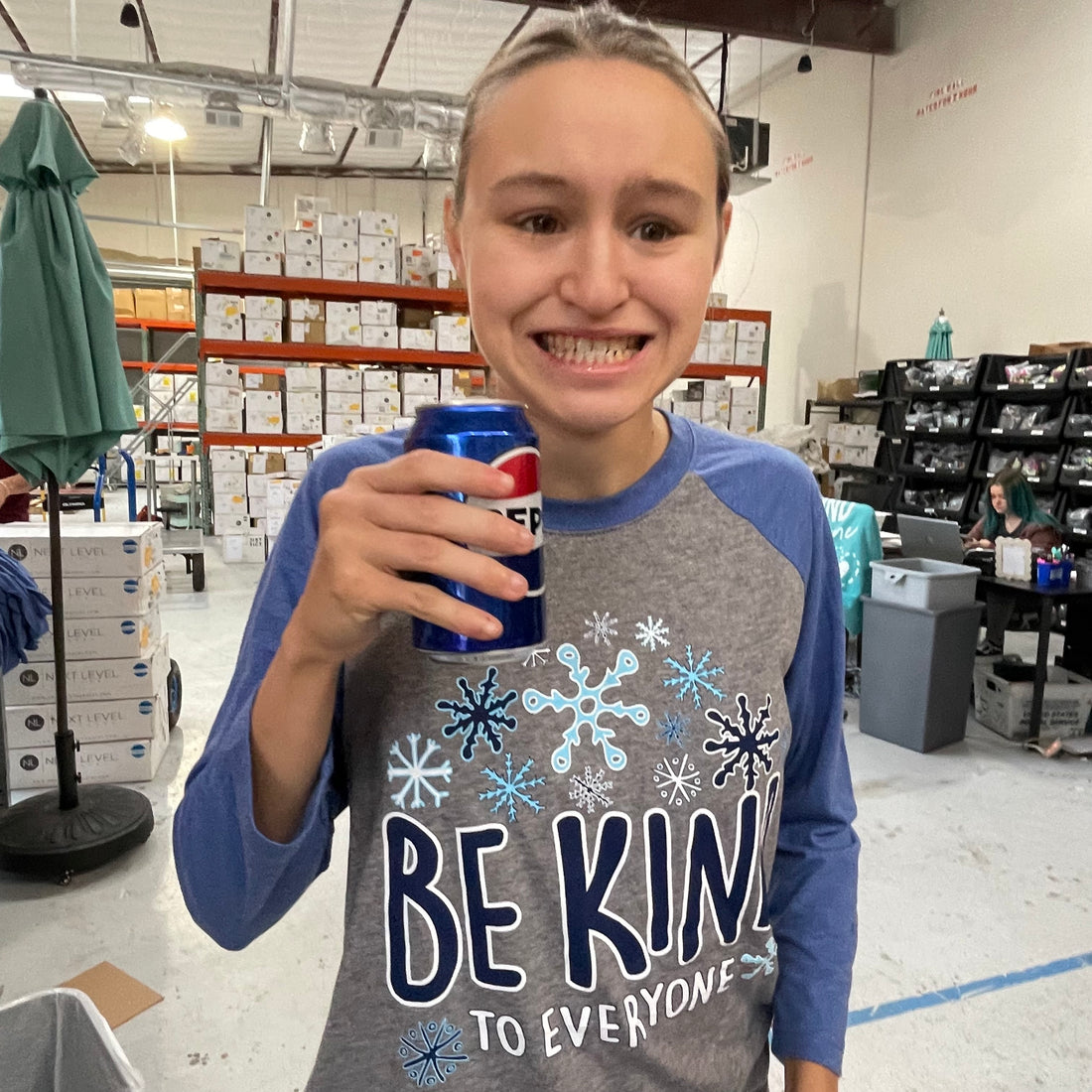 Jordyn, enjoying her favorite drink, while modeling a small in  our New Winter Be Kind to Everyone® Ragland Tee.