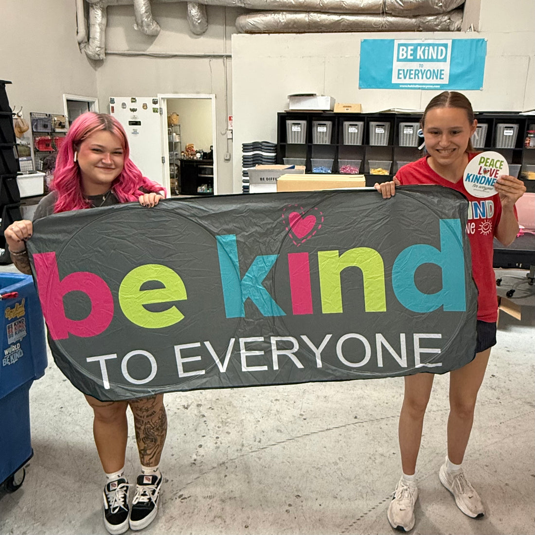 Sarah and Jordyn, at the Shirt Shop, displaying our Be Kind to Everyone® Car Sunshade and Peace, Love, and Kindness magnet.