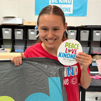 Jordyn, at the Shirt Shop, holding our Be Kind to Everyone® car sunshade and our Peace, Love, and Kindness for Everyone magnet.