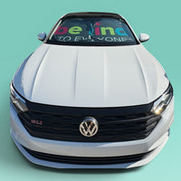 White Volkswagen car with  our Be Kind to Everyone® Car Sunshade against a teal background.  The car sunshade is gray with bright, multicolored text.
