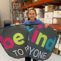 Jordyn, at the Shirt Shop, holding our Be Kind to Everyone® Car Sunshade. The car sunshade is gray with bright, multicolored text.