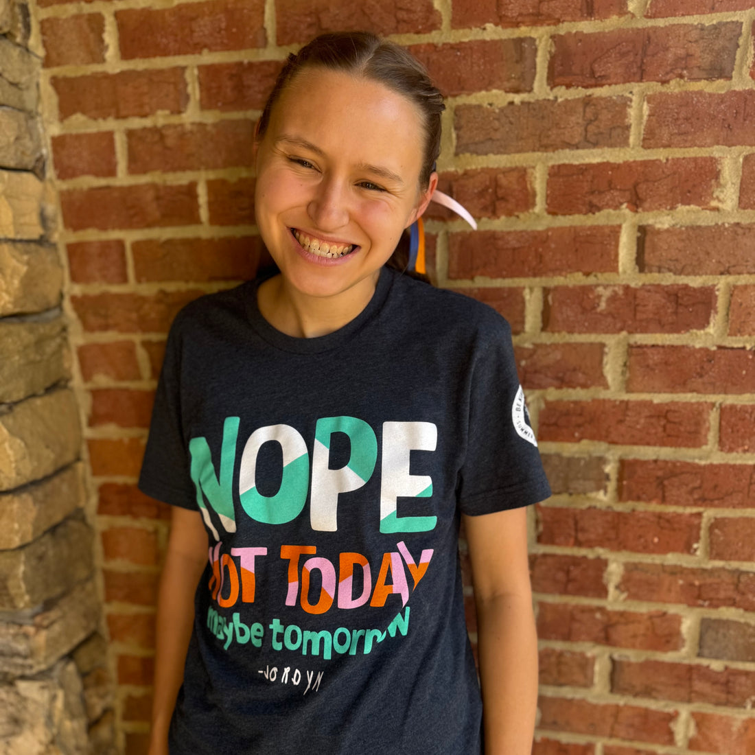 Jordyn, wearing our navy short-sleeved Nope Not Today t-shirt with a brick wall behind her.