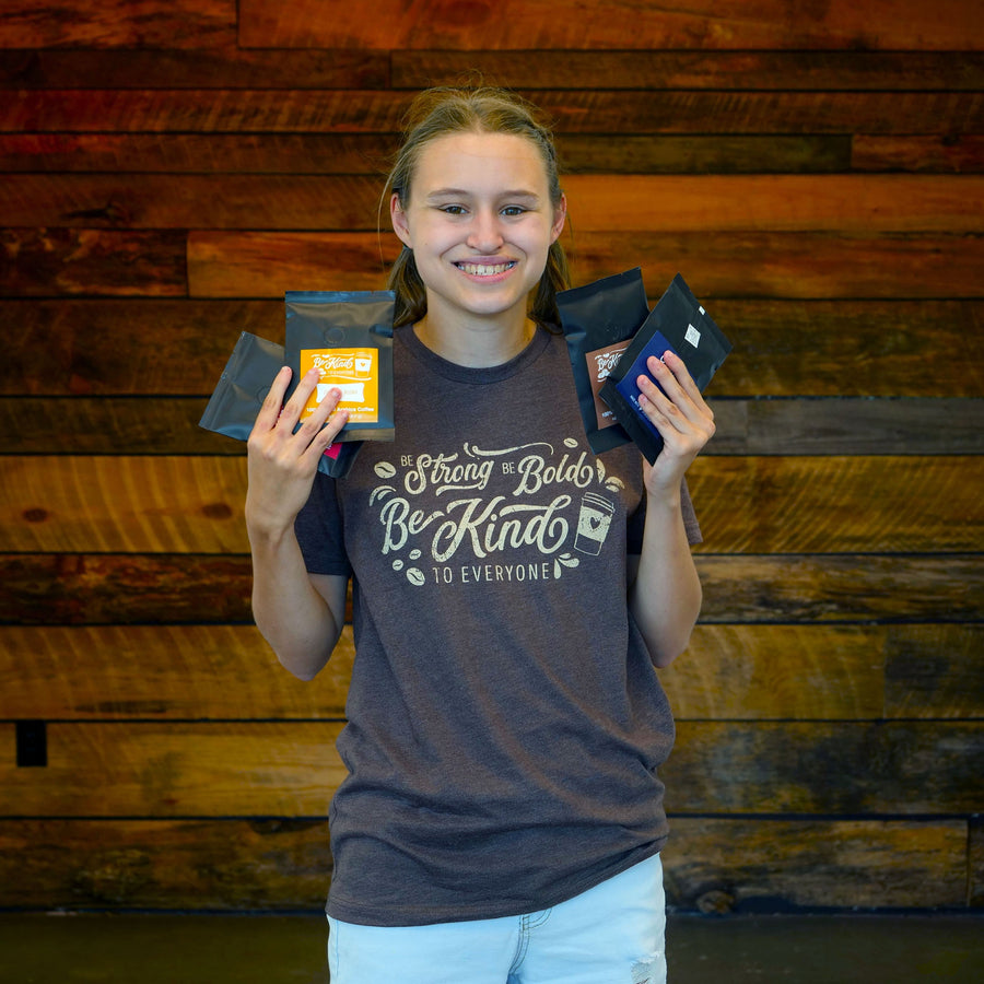 Jordyn, wearing our "Coffee" Be Kind to Everyone® shirt and holding some of our Coffee Sampler Packs.