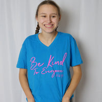 Jordyn wearing a small turquoise v-neck tee with Jordyn's Signature Be Kind to Everyone® design in pink.