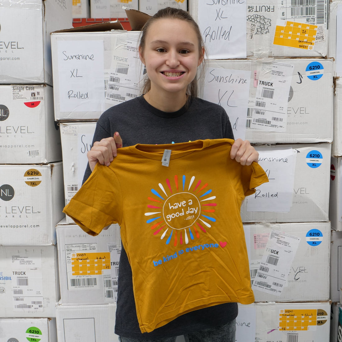 Jordyn holding up our new youth Sunshine Be Kind to Everyone® tee.