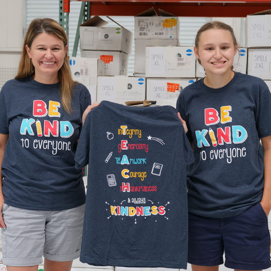 Jackie and Jordyn, at the shirt shop, displaying the back of our "T.E.A.C.H. Kindness" Be Kind to Everyone® short-sleeve tee.